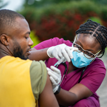 image of young african nurse in face mask, injecting young black man.